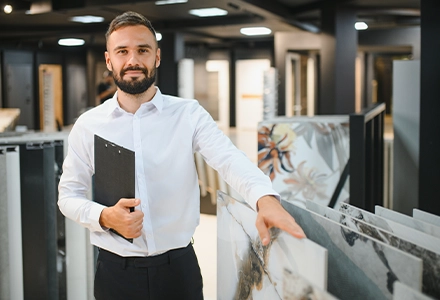 Man holding a clipboard in a showroom displaying tile or flooring samples, standing among product displays.