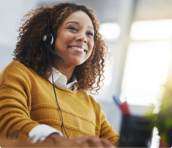Smiling customer service representative wearing a headset and working at a desk in an office environment.